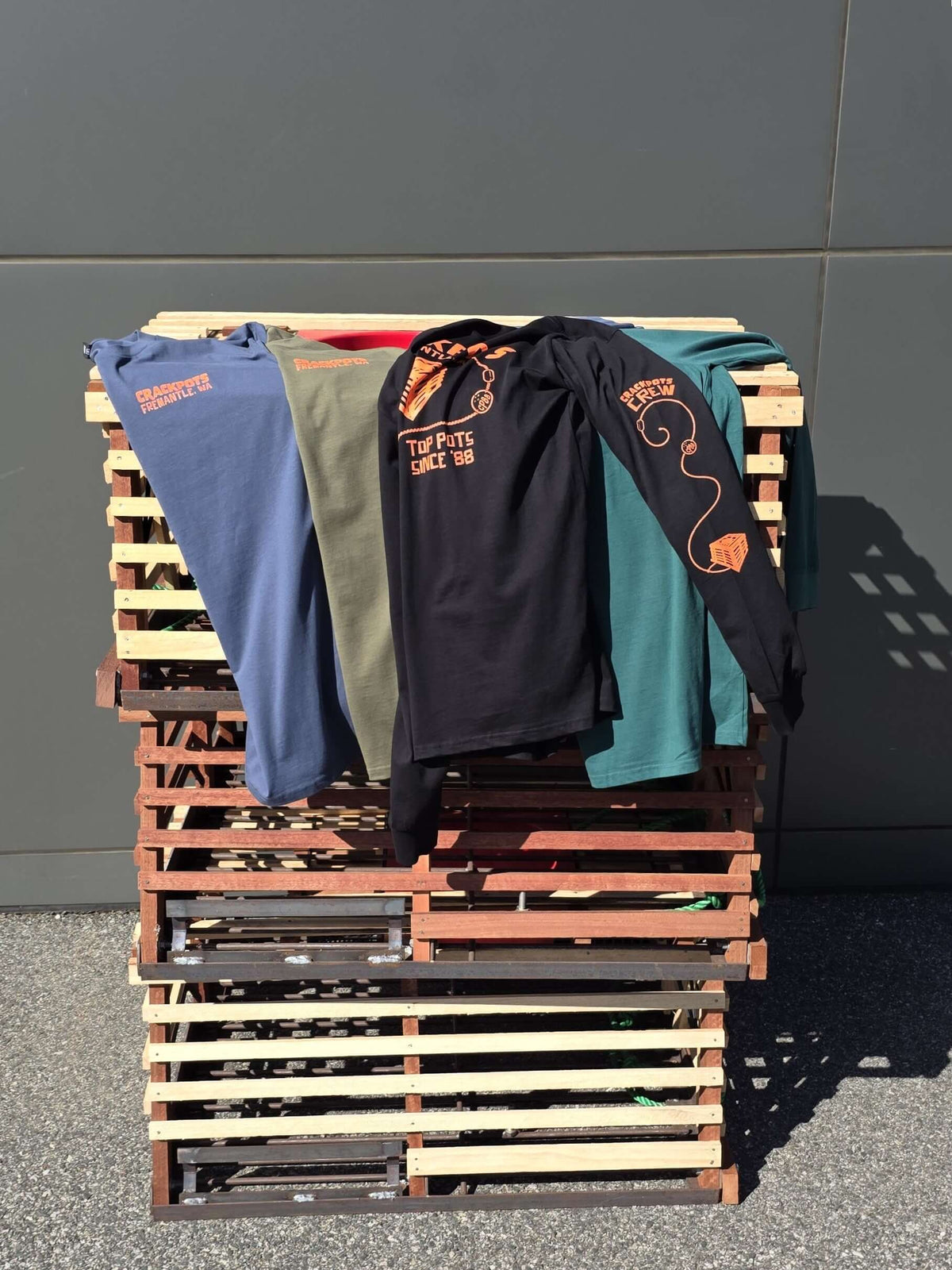 Crackpots Long Sleeve Tee - XL available in army green, jade green, black, and blue grey displayed on a wooden pallet.