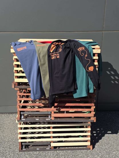 Crackpots Long Sleeve Tee -XXL displayed on wooden pallets in multiple colors for winter 2026 merchandise.