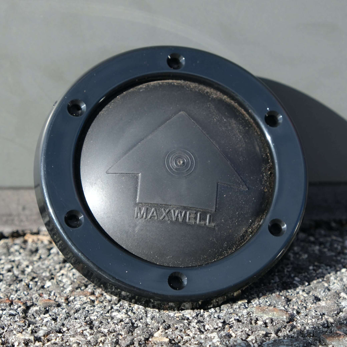 Maxwell FootSwitch Bezel Black resting on gravel surface with logo viewable.