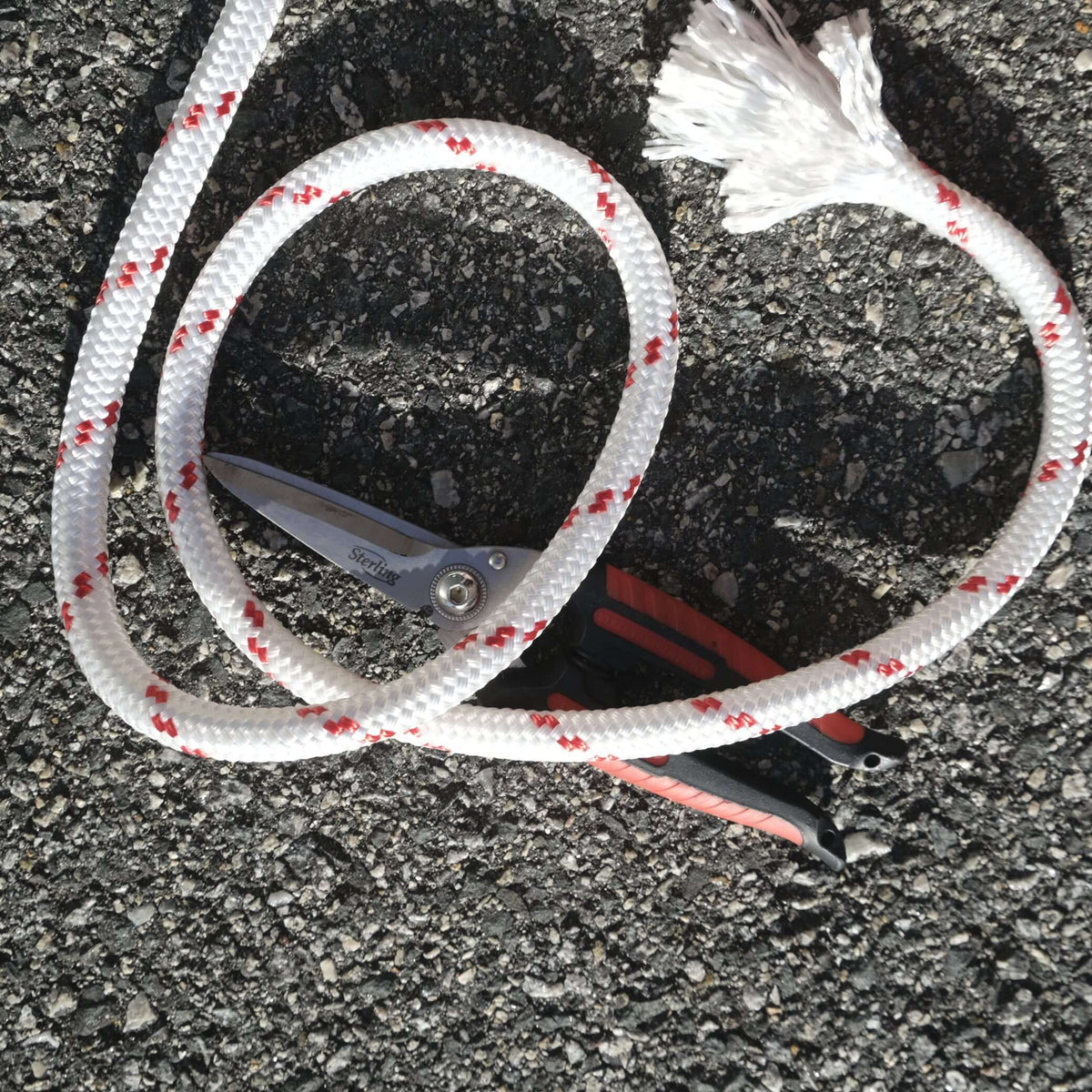 ROPE DB BRAIDED 12MM X M coiled on ground beside scissors, showcasing durability and strength for various applications.