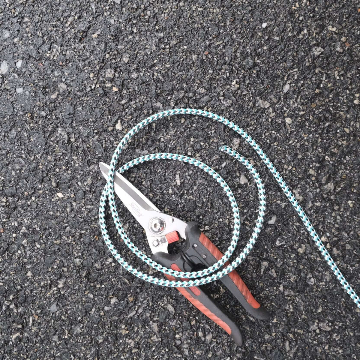 ROPE BR LEADCORE 5MM X M 45G with scissors on asphalt surface, showcasing its braided design for fishing applications.