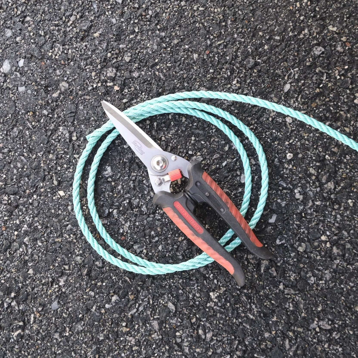 ROPE PP GREEN 6MM X 200M SPOOL coiled next to garden shears on asphalt surface.