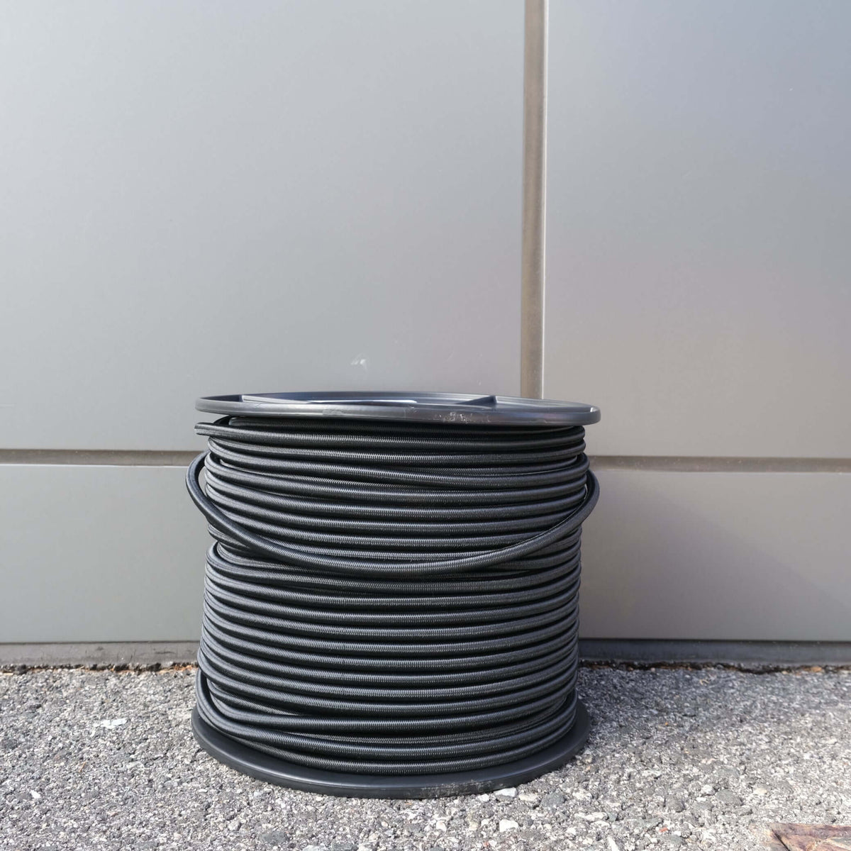 SHOCK CORD 7MM X 100M BLK coil on a spool, ideal for securing and fastening applications.