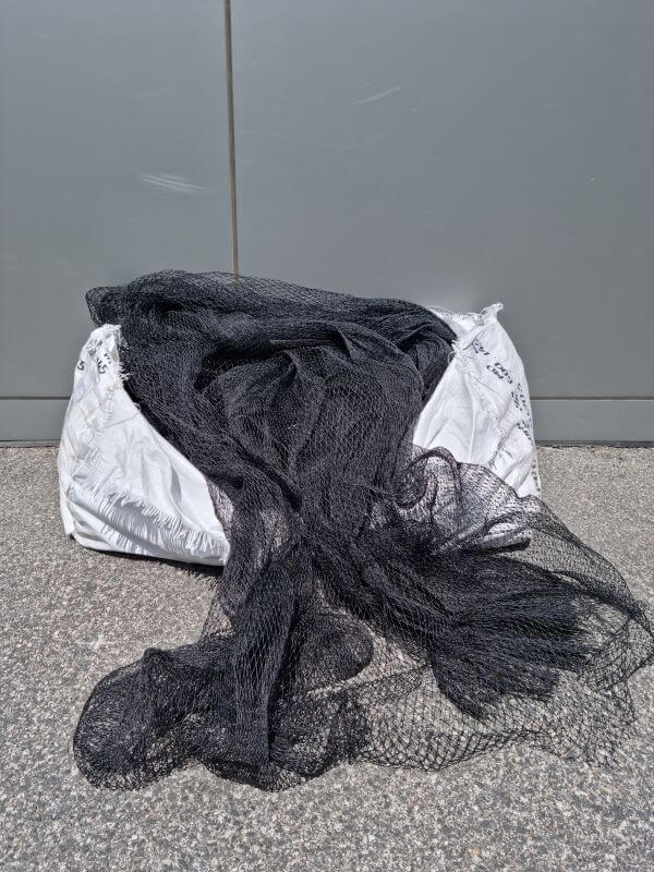 BIRD NET 6P 15M WIDE LINEAL M with black netting laid out over a bale on a concrete surface.