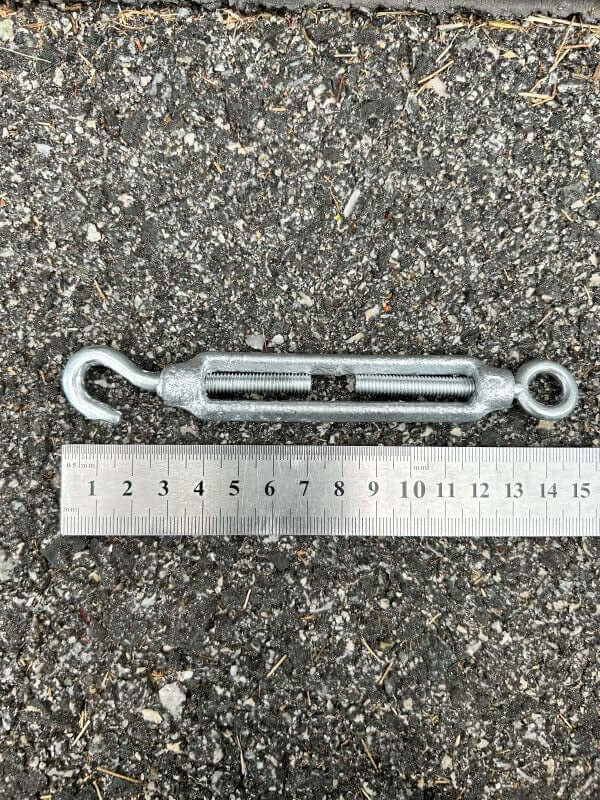 Galvanised TURNBUCKLE GALV 8MM with ruler on asphalt surface, ideal for tensioning ropes and cables.